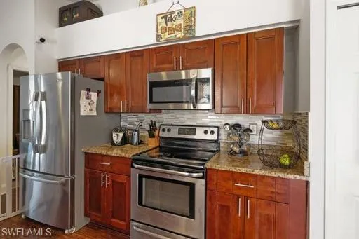 Kitchen featuring dark hardwood / wood-style floors, light stone countertops, stainless steel appliances, and tasteful backsplash