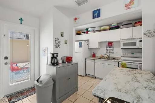 Kitchen with white appliances, backsplash, light tile floors, sink, and white cabinets