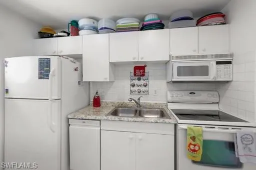 Kitchen featuring backsplash, white cabinetry, light stone countertops, sink, and white appliances