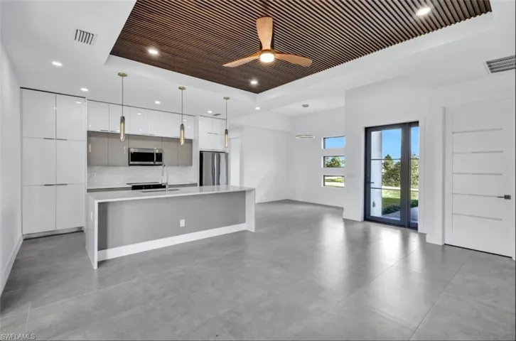 Kitchen featuring stainless steel appliances, white cabinetry, pendant lighting, a tray ceiling, and a kitchen island with sink