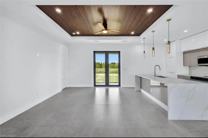 Kitchen featuring white cabinetry, light stone countertops, hanging light fixtures, sink, and a tray ceiling