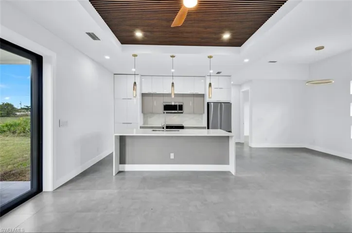 Kitchen featuring white cabinets, backsplash, a tray ceiling, pendant lighting, and appliances with stainless steel finishes