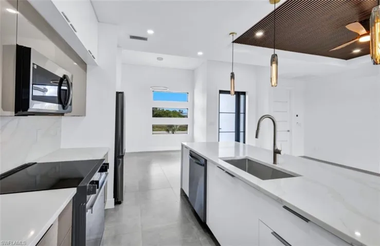 Kitchen with tasteful backsplash, appliances with stainless steel finishes, pendant lighting, sink, and white cabinets