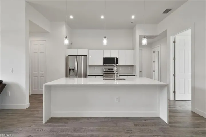 Kitchen with appliances with stainless steel finishes, white cabinetry, a sink, a spacious island, and light countertops
