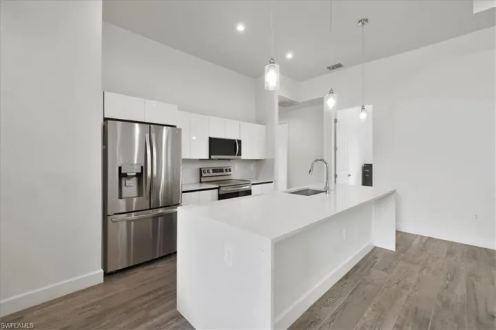 Kitchen with stainless steel appliances, a sink, white cabinetry, dark wood-style floors, and light countertops