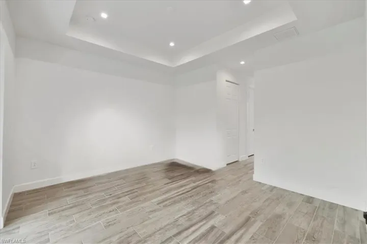 Spare room featuring a tray ceiling, light wood-type flooring, recessed lighting, and baseboards