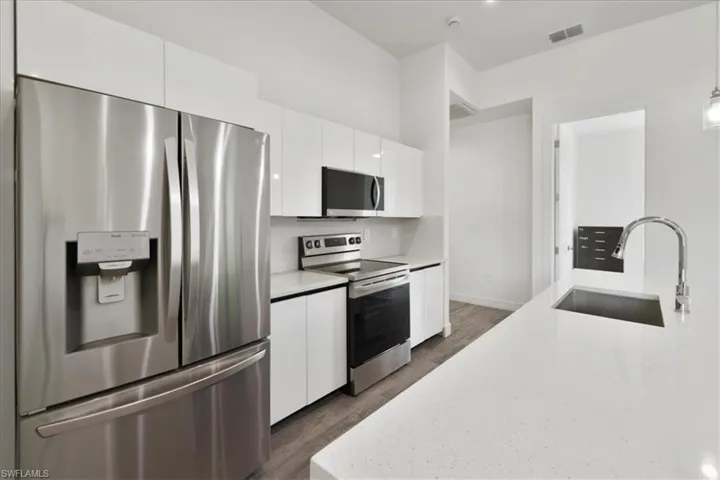 Kitchen featuring appliances with stainless steel finishes, a sink, dark wood-style floors, white cabinetry, and pendant lighting