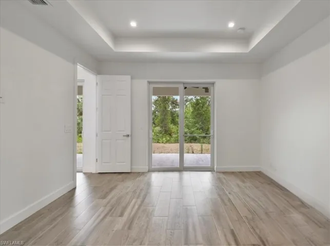 Spare room featuring a tray ceiling, light wood finished floors, baseboards, and recessed lighting