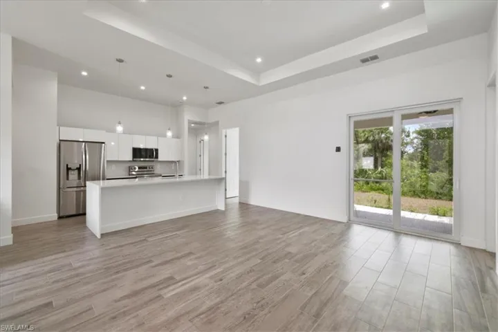 Unfurnished living room with a tray ceiling, light wood-style floors, recessed lighting, and a towering ceiling