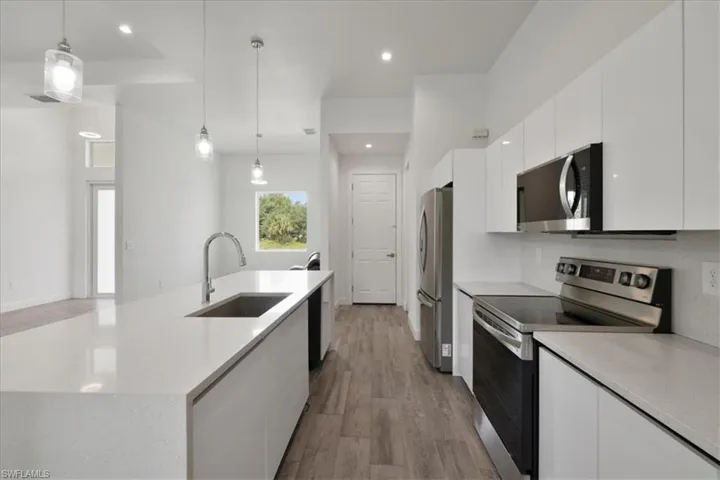 Kitchen with stainless steel appliances, a sink, a center island with sink, white cabinetry, and wood finished floors