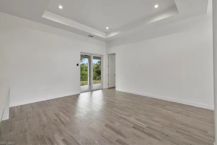Unfurnished room featuring a tray ceiling, recessed lighting, light wood-style flooring, and baseboards