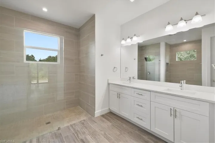 Full bathroom with a tile shower, plenty of natural light, double vanity, and wood tiled floors