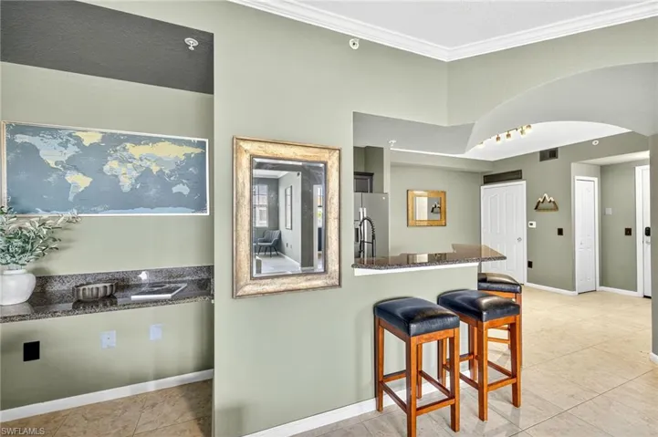 Kitchen featuring a breakfast bar area, light tile patterned floors, dark stone counters, ornamental molding, and arched walkways