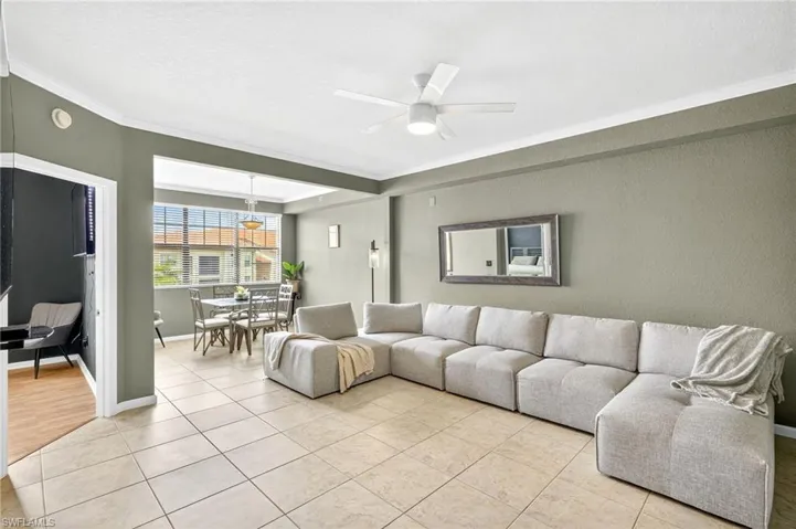 Living area featuring a ceiling fan, ornamental molding, light tile patterned floors, and a textured ceiling