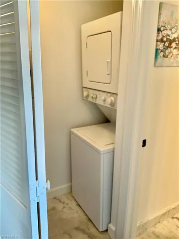 Clothes washing area featuring stacked washing maching and dryer and light tile patterned floors