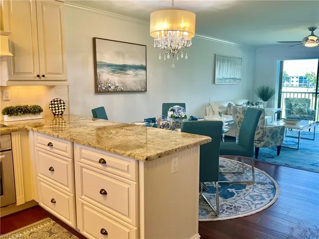 Kitchen featuring ceiling fan with notable chandelier, light stone countertops, kitchen peninsula, backsplash, and dark wood-type flooring