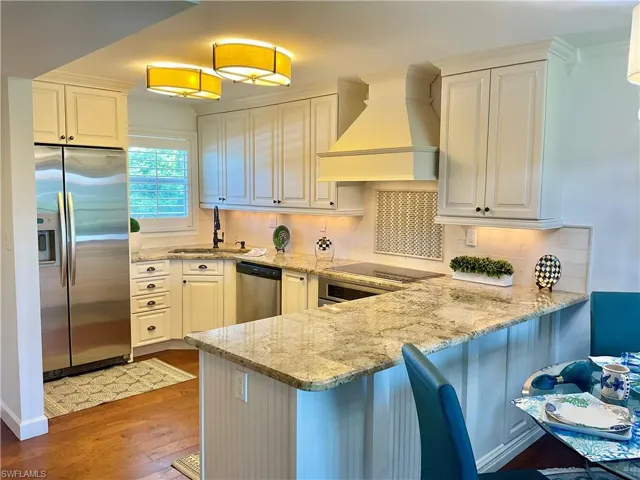 Kitchen with kitchen peninsula, premium range hood, stainless steel appliances, decorative backsplash, and wood-type flooring