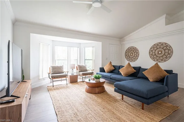 Living room with ceiling fan, hardwood / wood-style flooring, crown molding, and vaulted ceiling