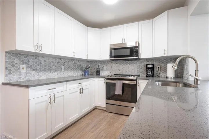 Kitchen with white cabinetry, stainless steel appliances, sink, light stone countertops, and light hardwood / wood-style floors