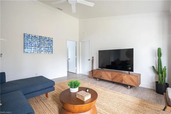 Living room with crown molding, ceiling fan, a towering ceiling, and hardwood / wood-style flooring