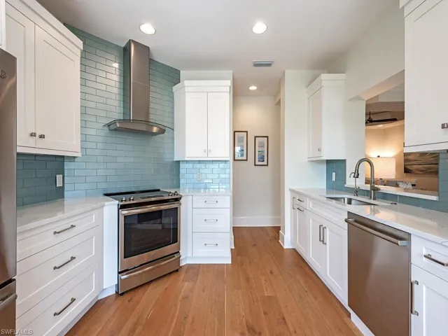 Kitchen with sink, light hardwood / wood-style flooring, wall chimney exhaust hood, appliances with stainless steel finishes, and white cabinetry