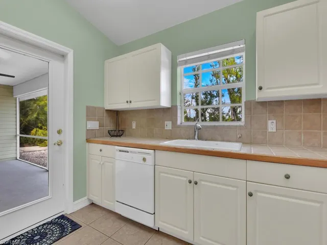 Kitchen featuring tile counters, sink, white dishwasher, decorative backsplash, and white cabinets