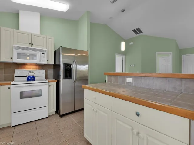 Kitchen featuring white cabinetry, tasteful backsplash, tile countertops, white appliances, and light tile patterned floors