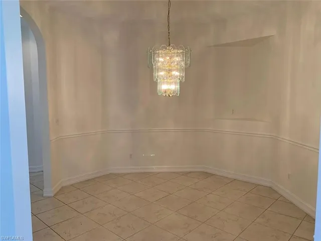 Unfurnished dining area featuring arched walkways, a chandelier, and light tile patterned flooring