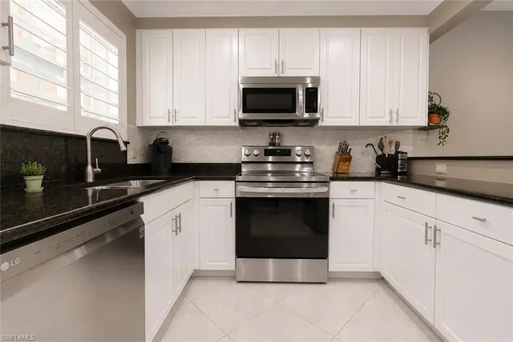 Kitchen featuring white cabinetry, dark stone countertops, stainless steel appliances, and a tile backsplash