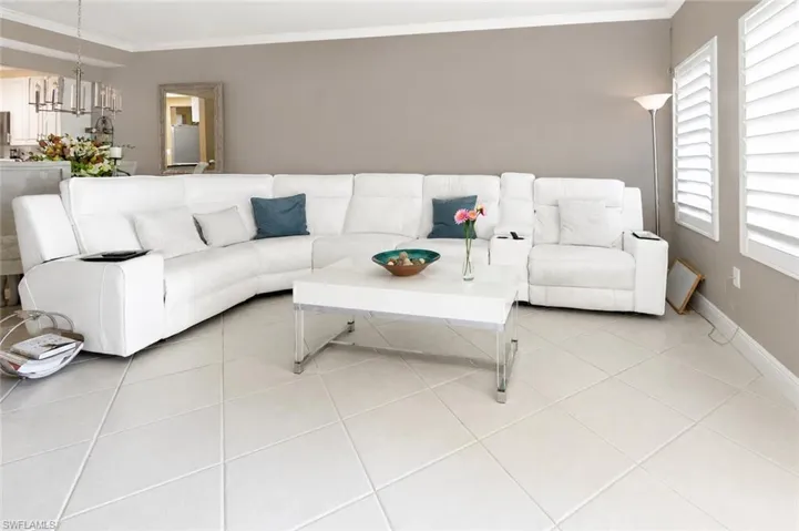 Living area featuring large format tile flooring, a neutral wall color, crown molding, and plantation shutters