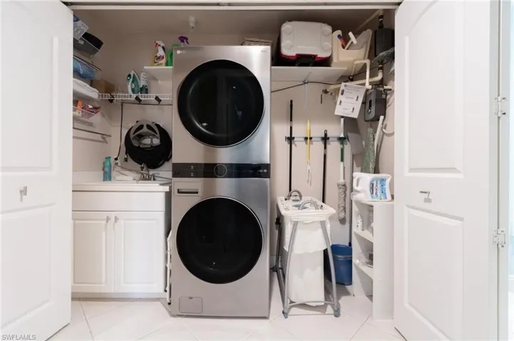 Laundry closet featuring cabinet space, stacked washer / drying machine, and light tile patterned flooring