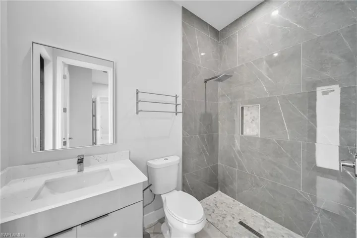 Bathroom featuring a tile shower, vanity, and toilet