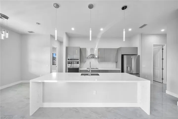 Kitchen featuring appliances with stainless steel finishes, hanging light fixtures, wall chimney exhaust hood, gray cabinets, and a large island