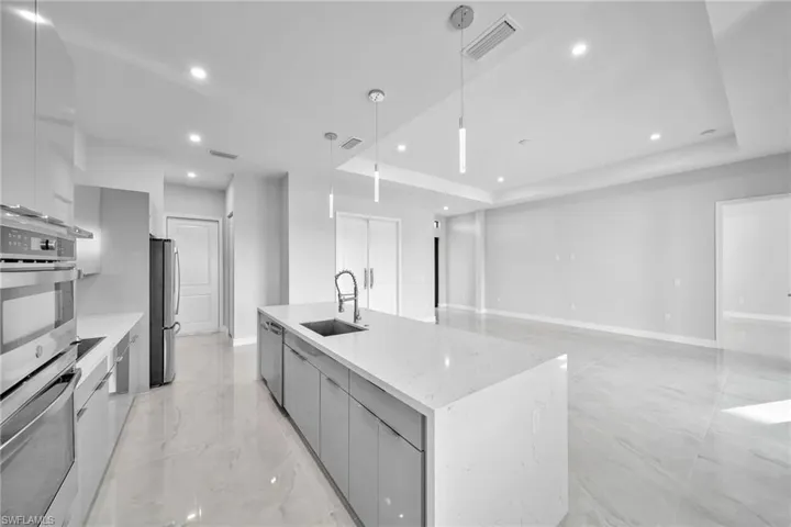 Kitchen featuring a raised ceiling, appliances with stainless steel finishes, hanging light fixtures, and a center island with sink