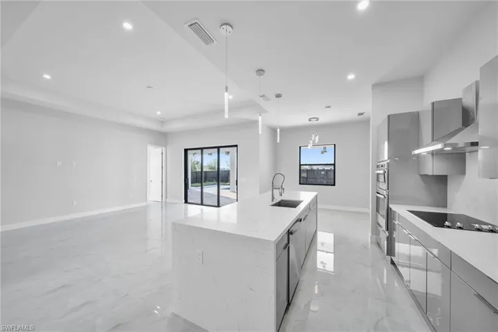Kitchen featuring pendant lighting, black electric stovetop, gray cabinets, sink, and an island with sink