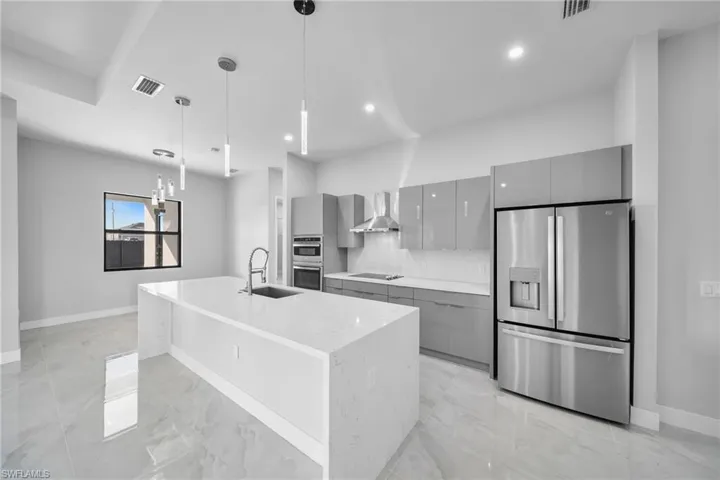 Kitchen with appliances with stainless steel finishes, wall chimney exhaust hood, gray cabinets, decorative light fixtures, and sink