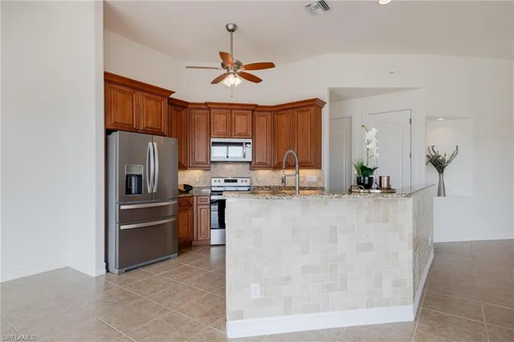 Kitchen featuring light tile patterned flooring, appliances with stainless steel finishes, decorative backsplash, light stone counters, and ceiling fan