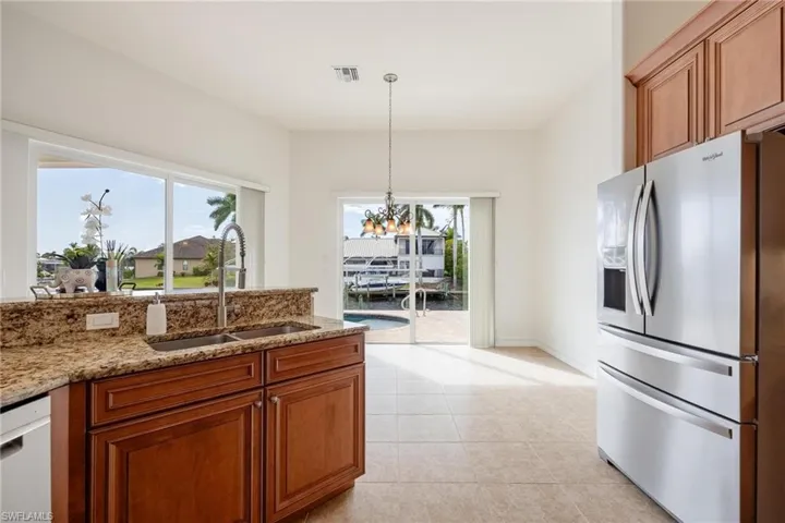Kitchen with dishwasher, stainless steel refrigerator with ice dispenser, sink, light stone counters, and light tile patterned floors