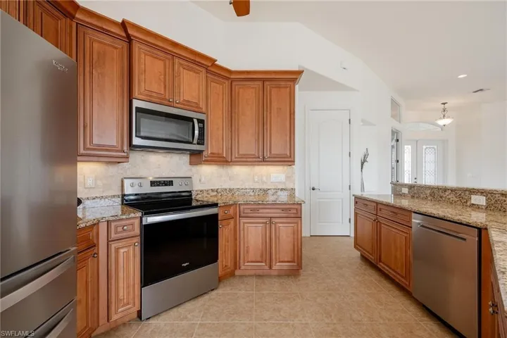 Kitchen with light tile patterned floors, stainless steel appliances, decorative backsplash, and light stone countertops