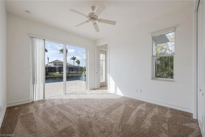Empty room with ceiling fan, light colored carpet, and a water view