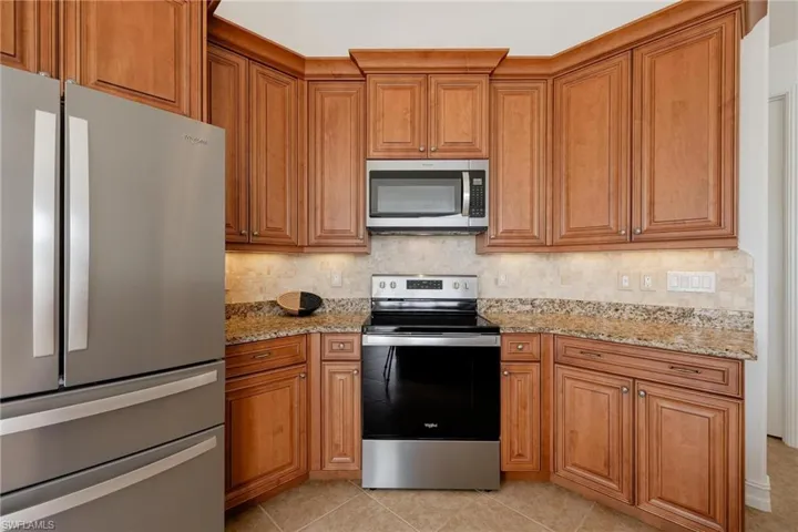Kitchen with decorative backsplash, appliances with stainless steel finishes, light stone counters, and light tile patterned floors