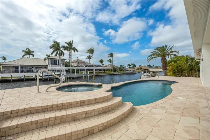 View of swimming pool featuring glass enclosure, a water view, an in ground hot tub, and a patio