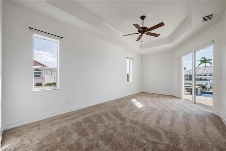 Carpeted spare room featuring ceiling fan, crown molding, and a tray ceiling