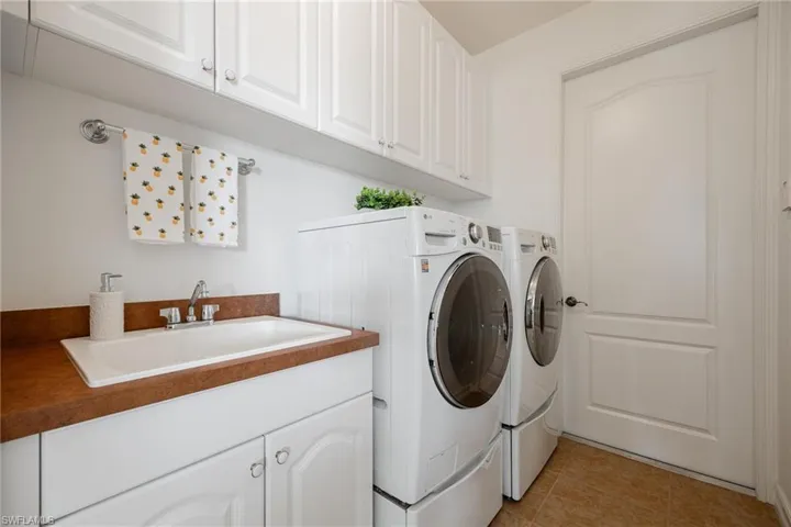 Laundry area featuring sink, washing machine and dryer, cabinets, and light tile patterned floors
