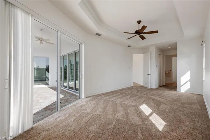 Empty room featuring ceiling fan, a raised ceiling, and light carpet