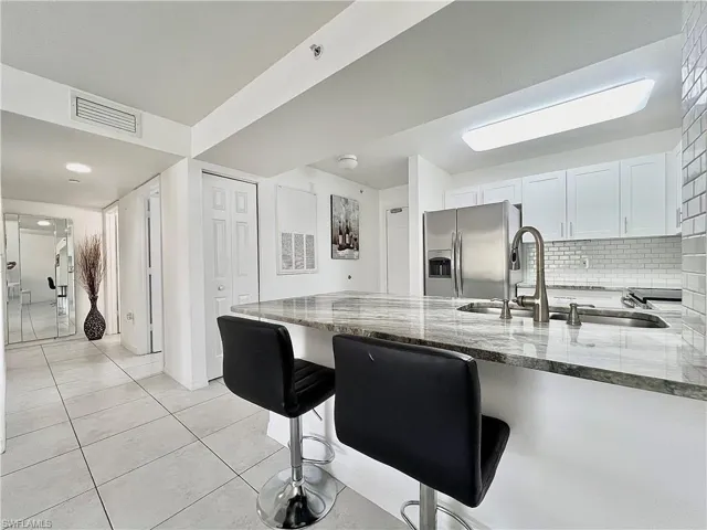 Kitchen featuring stainless steel fridge, white cabinets, dark stone counters, tasteful backsplash, and light tile floors