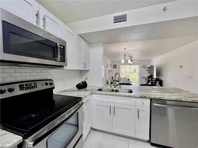 Kitchen with stainless steel appliances, tasteful backsplash, white cabinetry, sink, and light tile floors