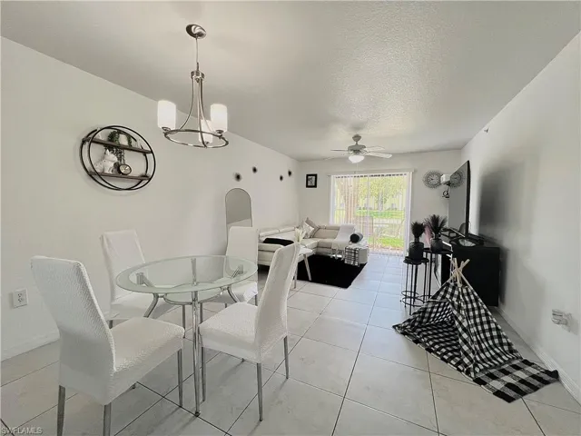 Dining space featuring ceiling fan with notable chandelier and light tile flooring