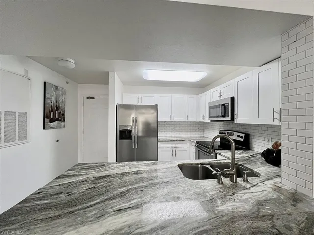 Kitchen with sink, stainless steel appliances, backsplash, and white cabinetry