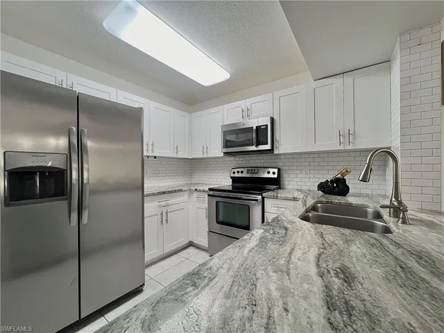 Kitchen featuring stainless steel appliances, white cabinets, backsplash, and light tile floors